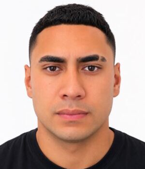 Close-up portrait of a young man with short black hair, brown eyes, and a neutral expression against a white background.