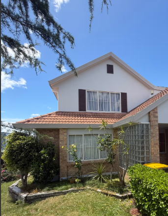White two-story house with a red-tiled roof and brick accents, front garden and blue sky above.