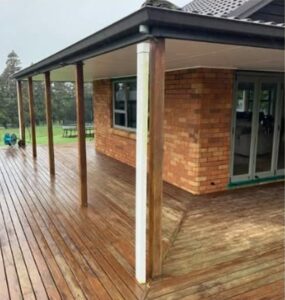 Wooden deck wrapping a brick house, supported by posts under a covered patio area.